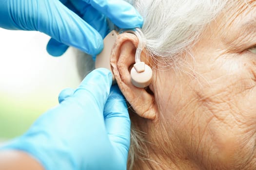 Doctor install hearing aid on senior patient ear to reduce hearing loss problem.