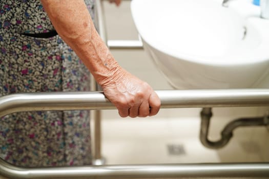 Asian elderly old woman patient use toilet support rail in bathroom, handrail safety grab bar, security in nursing hospital.