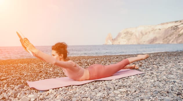 Middle aged well looking woman with black hair doing Pilates with the ring on the yoga mat near the sea on the pebble beach. Female fitness yoga concept. Healthy lifestyle, harmony and meditation.