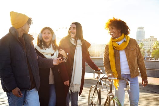 Group of happy multiracial friends laughing together while walking around city harbour on a sunny winter day. College student and lifestyle concept.