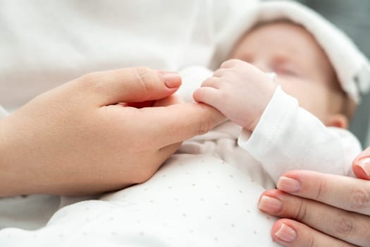Close-up displays a sick newborn baby tenderly gripping mother's finger, wet towel resting on its forehead