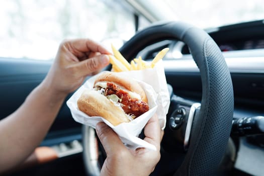 Asian woman driver hold and eat hamburger in car, dangerous and risk an accident.