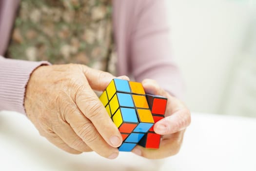 Bangkok, Thailand - May 15, 2022 Asian elderly woman playing Rubik cube game to practice brain training for help dementia prevention and Alzheimer disease.