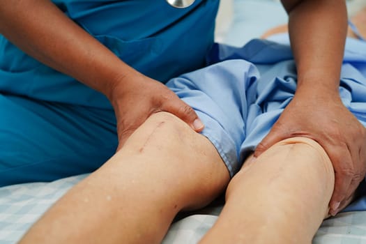 Doctor checking Asian elderly woman patient with scar knee replacement surgery in hospital.