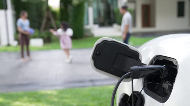 Progressive parent have returned from picking up daughter at school with concept of electric vehicle and renewable energy, charging station for EV car at home. Alternative eco transportation.