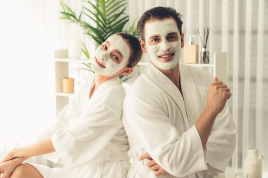 Blissful couple in bathrobe with facial cream mask enjoying serene ambiance of spa salon resort or hotel during holiday. Pampering face spa and skincare treatment with essence relaxation. Quiescent