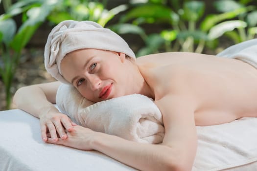 A beautiful young woman lies on a spa bed while looking at camera. Feeling of relaxed and at peace. Attractive caucasian woman surrounded by the calming sounds of nature. Tranquility