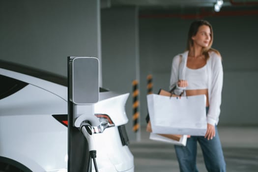 Young woman travel with EV electric car to shopping center parking lot charging in downtown city showing urban sustainability lifestyle by green clean rechargeable energy of electric vehicle innards