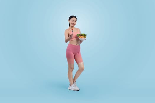 Young sporty Asian woman in sportswear holding salad bowl fill with vibrant of fruit and vegetable. Natural youthful and fit body lifestyle with balance nutrition on isolated background. Vigorous