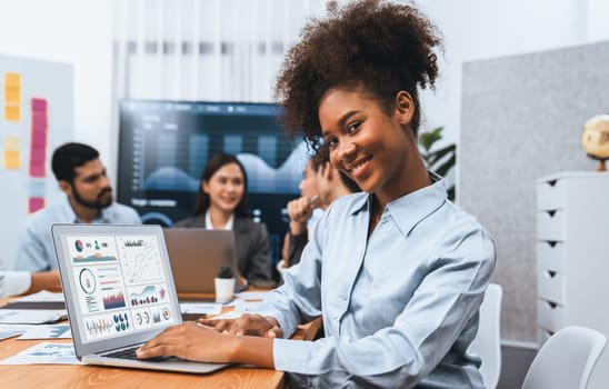 Portrait of happy young african businesswoman with group of office worker on meeting with screen display business dashboard in background. Confident office lady at team meeting. Concord