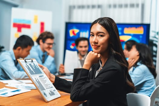 Portrait of happy young asian businesswoman or analyst looking at camera with her colleague analyzing data analysis in dynamic business strategy investment planning meeting. Habiliment