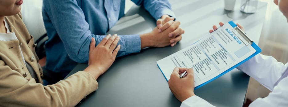 Doctor providing compassionate healthcare consultation while young couple patient holding hand, comfort each other after infertile report. Reproductive and medical fertility consulting. Neoteric