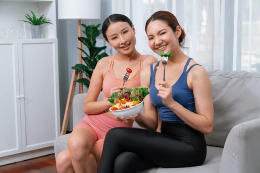 Young sporty Asian women in sportswear holding salad bowl together fill with vibrant of fruit and vegetable. Natural youthful and fit body lifestyle with balance nutrition and home exercise. Vigorous