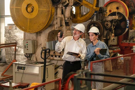 Factory engineer manager with assistant using laptop to conduct inspection of steel industrial machine, exemplifying leadership as machinery engineering inspection supervisor in metalwork manufacture.