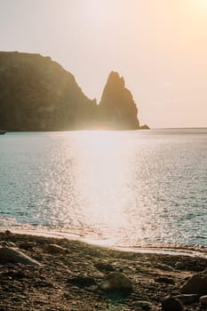 A red burning sunset with the silhouette of a cliff over the sea. Abstract nature summer or spring ocean sea background. Small waves on golden warm water surface with bokeh lights from sun.