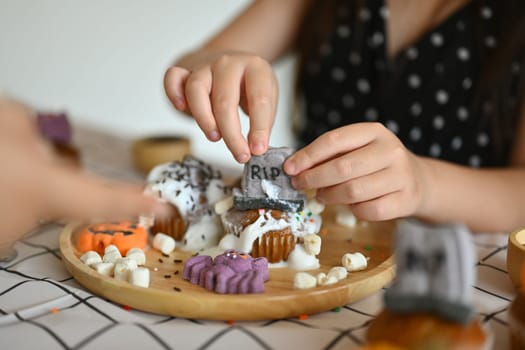 Cropped shot of little girl decorating Halloween cupcakes, preparing for holiday party in kitchen.