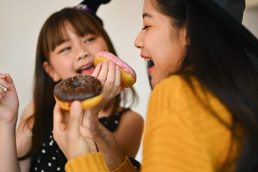 Happy family, cute little girl eating sweet donut with mother in kitchen. Halloween celebration and activity relationship in house.