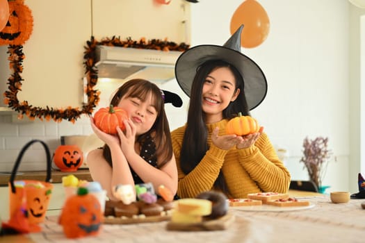 Happy mother and cute girl daughter are having fun preparing Halloween desserts in kitchen.