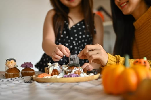 Cropped shot of little girl decorating Halloween cupcakes with different monsters, pumpkins and ghosts.