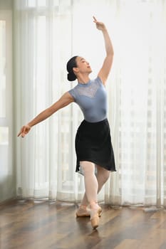 Full length beautiful ballerina dancing with graceful hands near window in studio. Dance, art and education concept.