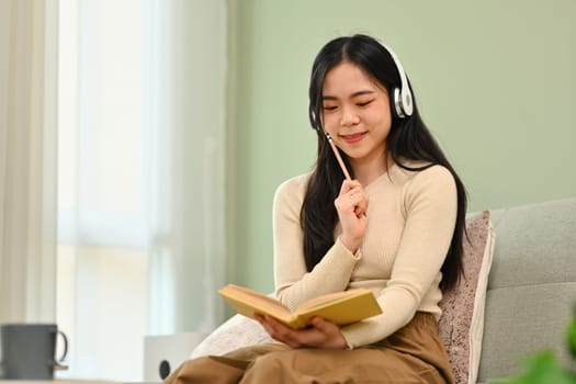 Pretty young woman wearing headphone writing notes, planning workday in personal paper organizer.