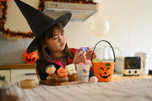 Adorable little girl decorating Halloween cupcakes with different monsters, pumpkins and ghosts.