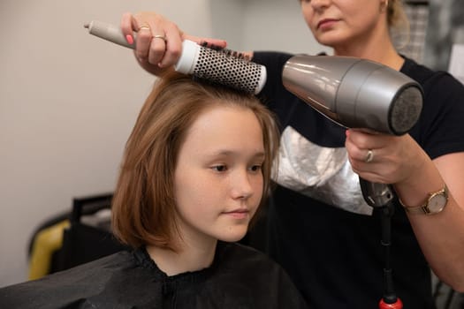 A professional stylist skillfully using a blow dryer and a brush to style a young girls hair inside a salon