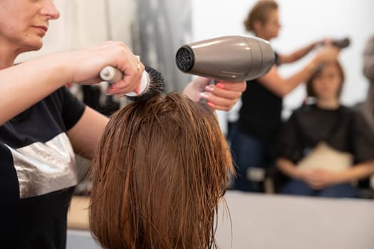 In a modern salon, a skilled stylist carefully uses a professional hair dryer on freshly washed hair