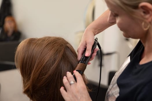 A talented stylist is expertly curling a clients hair, highlighting exceptional creativity and skill in hair care
