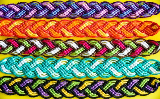 Selective focus of multi-colored woven DIY friendship bracelets Pigtail handmade of embroidery bright thread with knots on yellow background