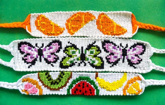 Three white woven DIY friendship bracelets handmade of embroidery bright thread with knots. Alpha weaving with fruit and butterflies patterns