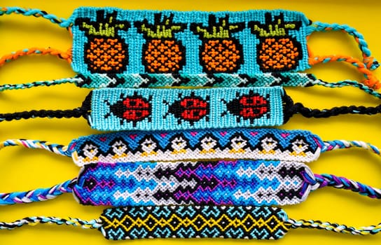 Many tied woven DIY friendship bracelets handmade of embroidery bright thread with knots on yellow background. Alpha and normal patterns