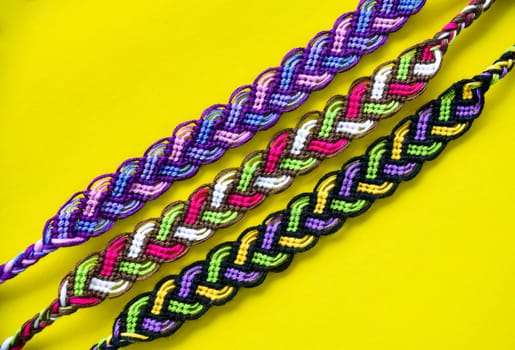 Many tied woven DIY friendship bracelets handmade of embroidery bright thread with knots on yellow background. Alpha and normal patterns