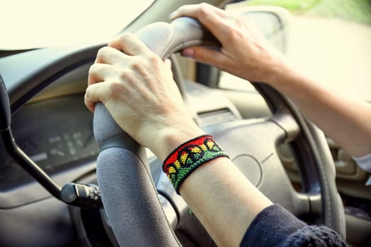 Handmade DIY friendship bracelet with Rasta flag pattern with a peace symbol on womens wrist. Hands holding steering wheel in the car.