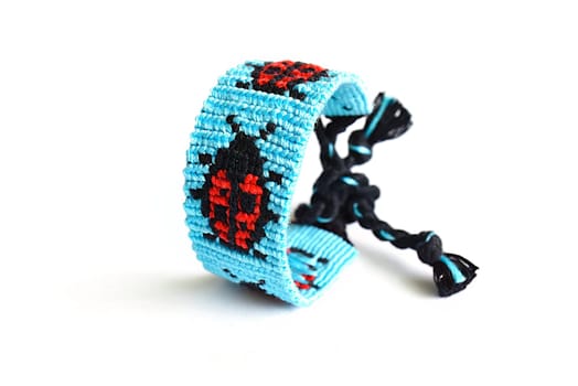 Selective focus of tied woven DIY friendship bracelet with alpha pattern Ladybug handmade of embroidery bright thread with knots isolated on white background