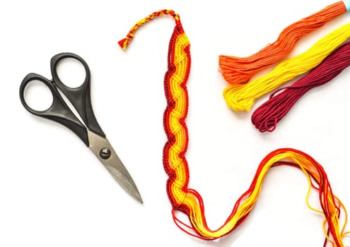 Unfinished woven DIY friendship bracelet with boho pattern next to scissors on white background