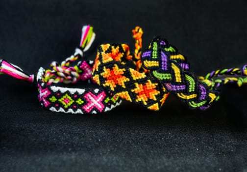 Woven DIY friendship bracelets handmade of embroidery bright thread with knots on black background.