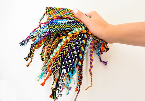 Female hand holding many woven multi-colored DIY friendship bracelets handmade of embroidery thread with knots on white background.