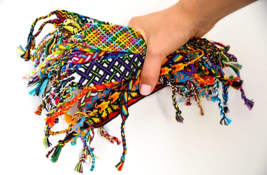 Female hand holding many woven multi-colored DIY friendship bracelets handmade of embroidery thread with knots on white background.