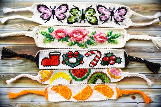 Woven colorful friendship bracelets with alpha patterns: butterflies, roses, christmas, oranges and fruits. Handmade of thread on wooden background. DIY gift idea