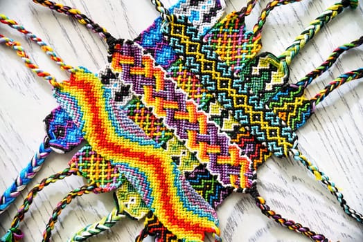 Woven DIY friendship bracelets handmade of embroidery bright thread with knots on table.