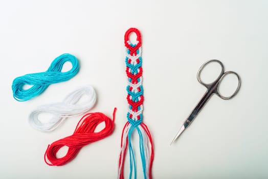 Unfinished woven DIY friendship bracelet with boho pattern next to scissors on white background
