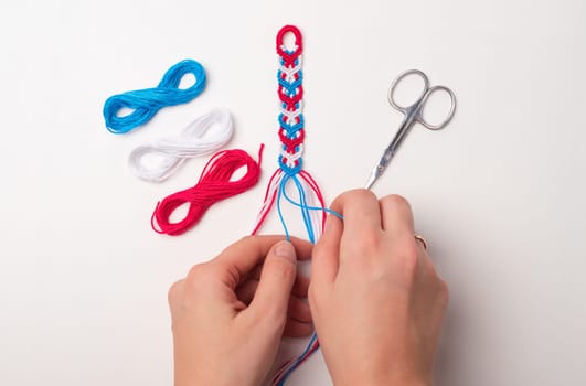 Process of weaving knot for DIY friendship bracelet. Female hands. step by step. White background with copy space, scissors and thread