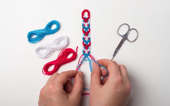 Process of weaving knot for DIY friendship bracelet. Female hands. step by step. White background with copy space, scissors and thread