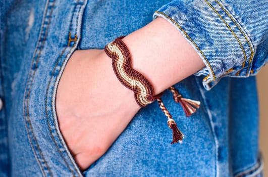 DIY woven tied friendship bracelet on a wrist. Hand in pocket