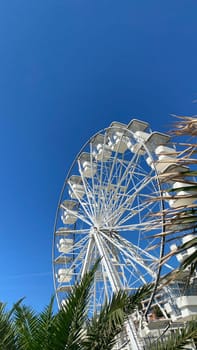 White Ferris wheel against bright blue sky, seen from below