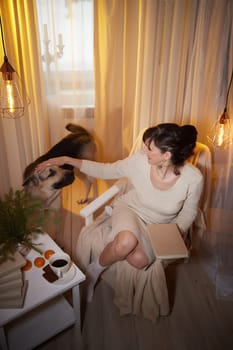 A middle-aged woman relaxes in a cozy apartment, petting her dog by soft light while enjoying a quiet evening.