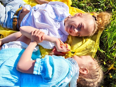 Two joyful children share apples and laughter while relaxing on a bright yellow blanket in a sunny park.