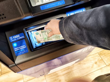 Kirov, Russia - September 29, 2024: Individual inserting a banknote into an ATM machine to withdraw cash in a busy area during daylight hours.