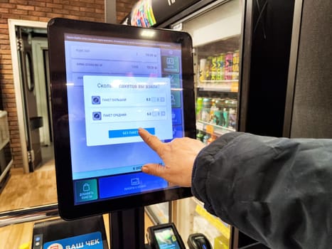 Kirov, Russia - December 03, 2024: Shoppers use a touchscreen to weigh products and manage payments at a self-service checkout station in a retail environment.